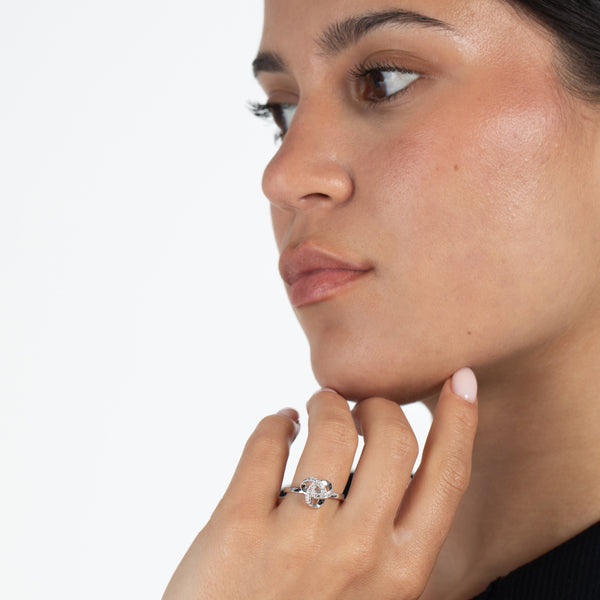 Close-up of a woman wearing a diamond  and sterling silver love knot ring on a plain background